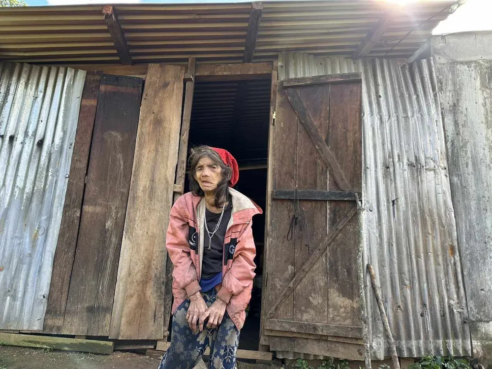 Cụ bà Y Buah bên căn nhà của bà Cụ bà Y Buah bên căn nhà của bà