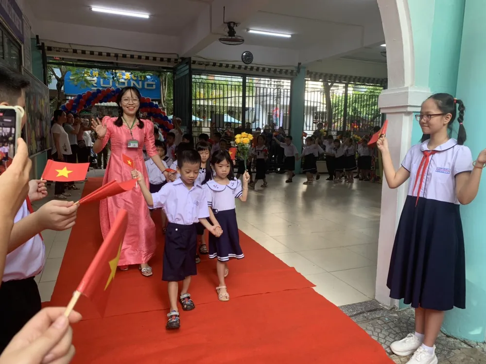 Các em lớp 1 cầm hoa và cờ được cô giáo dẫn vào sân trường. Ảnh: XUÂN QUỲNH