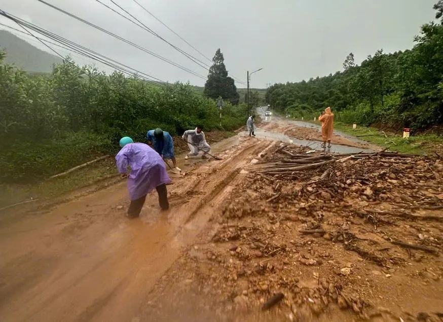 Lực lượng chức năng xử lý đất đá sạt lở, cây gỗ tràn ra đường. Ảnh: LÊ PHÚ NGUYỆN