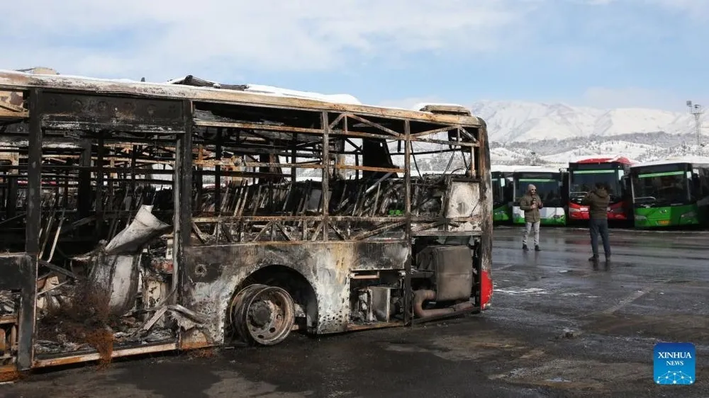 Các phóng viên truyền thông đang tác nghiệp bên cạnh một chiếc xe buýt bị phá hủy trong cuộc bạo loạn gần đây ở Tehran, Iran, ngày 21-1. Ảnh: THX