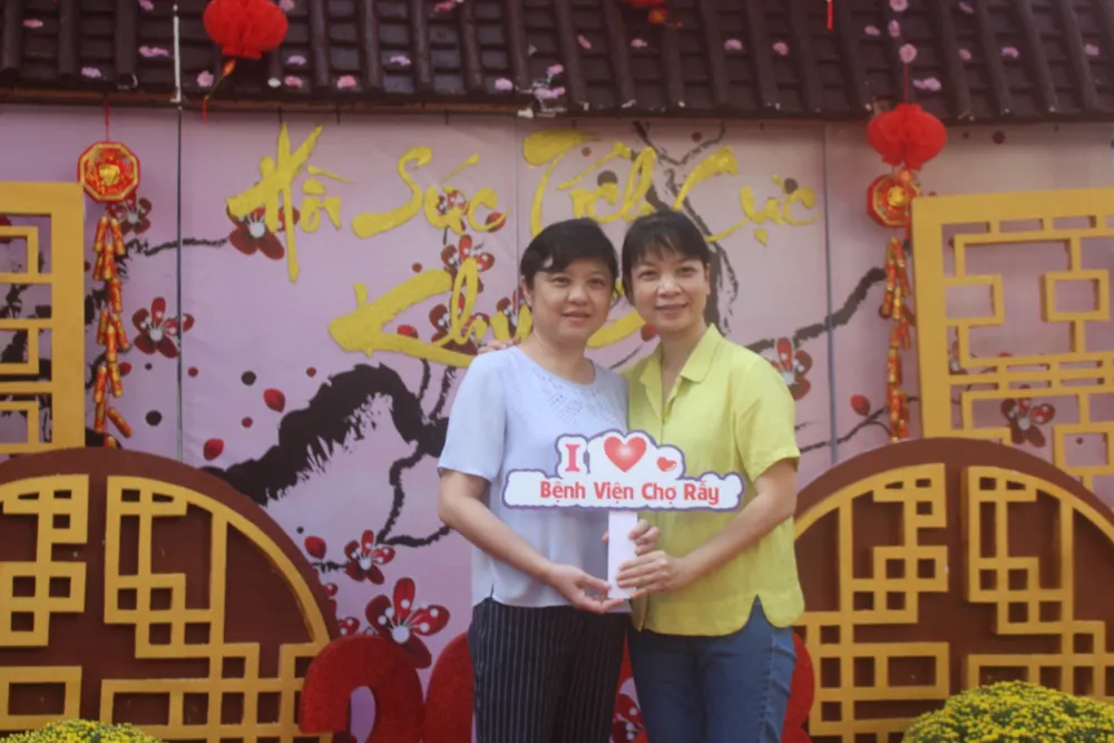 Bệnh nhân và người nhà vui vẻ tạo dáng bên đường hoa được các nhân viên y tế xây dựng trong khuôn viên bệnh viện