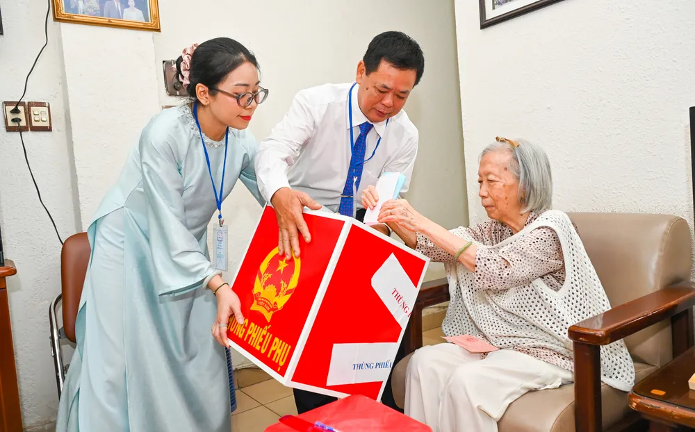 Cử tri Nguyễn Thị Kim Lan, 91 tuổi, được các thành viên tổ bầu cử số 7, phường Tân Định đưa thùng phiếu phụ đến tận nhà để thực hiện bầu cử. Ảnh MẠNH THẮNG.jpg