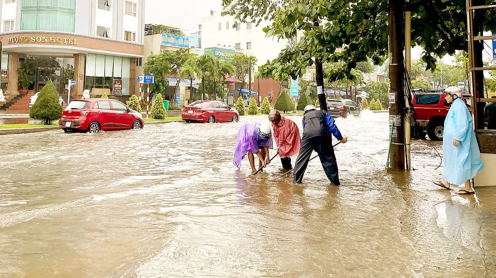 Người dân cậy nắp, dọn rác khơi thông miệng cống tại đường Cách Mạng Tháng Tám - Nguyễn Hữu Thọ (quận Cẩm Lệ, Đà Nẵng). Ảnh: PHẠM NGA