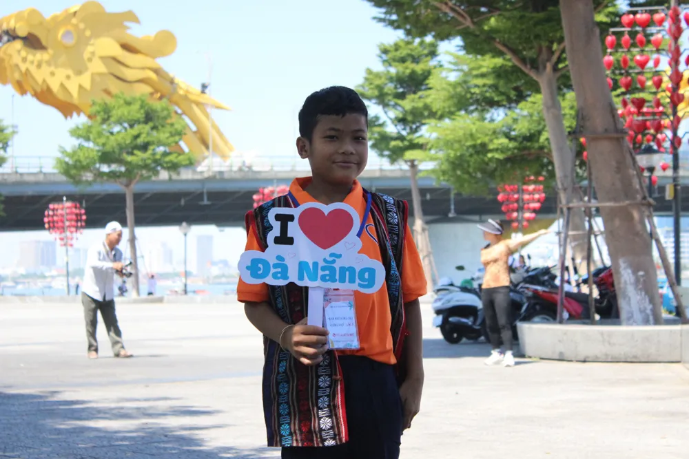 Được check in bên cầu Rồng, em Hồ Văn Nhí không giấu được niềm vui của mình mà thốt lên rằng: "Cây cầu này đẹp quá, cô ơi!". Nói xong, em liền chỉnh trang lại bộ quần áo để các cô chú trong đoàn ghi lại hình ảnh đáng nhớ này. Ảnh: PHẠM NGA