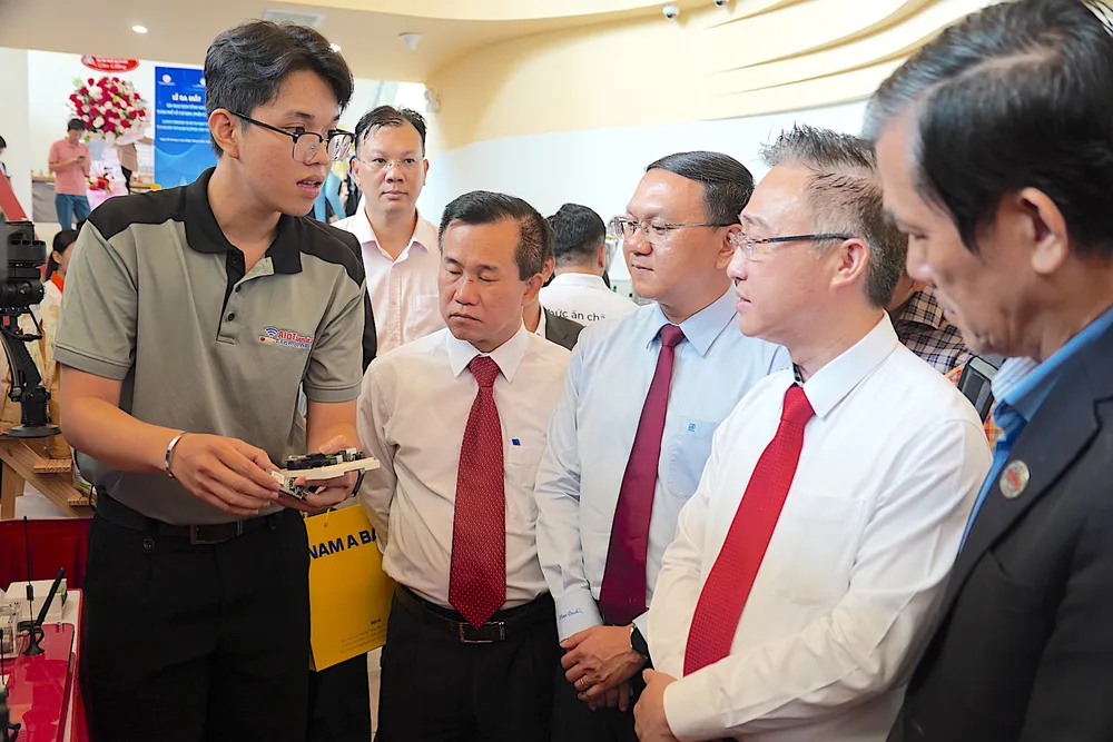 Đồng chí Đặng Minh Thông (thứ 2 từ phải sang) nghe đại diện Trường Đại học Kỹ thuật công nghệ giới thiệu về chip thiết kế vi mạch do trường nghiên cứu, sáng chế. ẢNH QUANG HUY