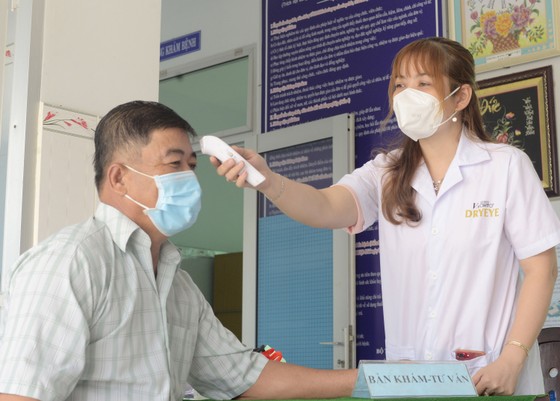 Chị Hồng Gấm đo thân nhiệt cho người dân đến khám chữa bệnh tại Trạm y tế xã An Ngãi Trung