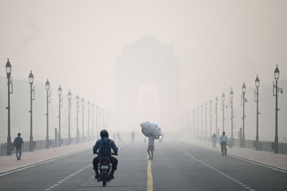 当地时间2022年11月1日，印度新德里，雾霾天里，一名男子背着麻袋走在印度门附近的路上。（图：AFP）