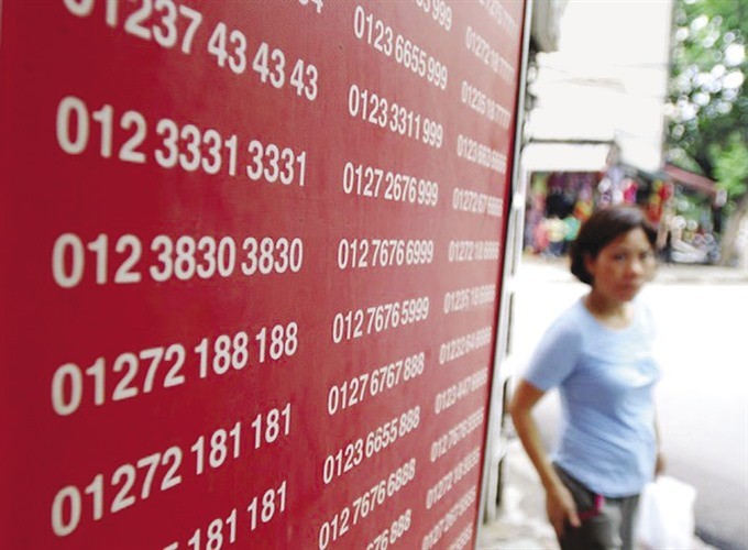 A woman walks past a board showing telephone numbers on sale. (Photo: laodong.vn)